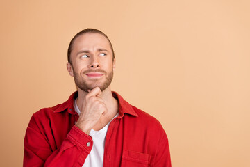 Portrait of nice young man look empty space think wear red shirt isolated on beige color background