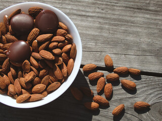 Almonds and dark chocolate in a bowl on a wooden table. Healthy snack.