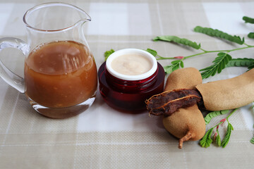 Lotion mixed with tamarind in a red jar, placed between a glass pitcher of concentrated tamarind...
