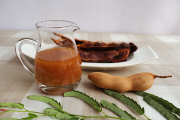 Glass jar with concentrated tamarind juice. Ripe fruit is placed on the side and peeled on a plate...