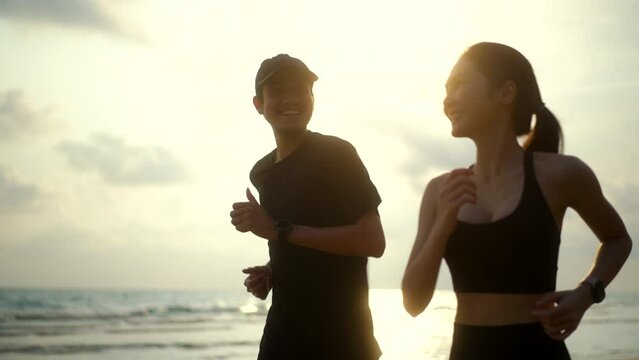 Young couple wearing sportswear running on sand sea ocean beach outdoor. Couple young two friends running or jogging at seaside for healthy lifestyle. Training athlete work out outdoor concept.