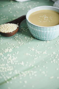 Pretty bowl filled with tahini sauce with copy space. Wooden spoon overflowing with sesame seeds. Top view. 