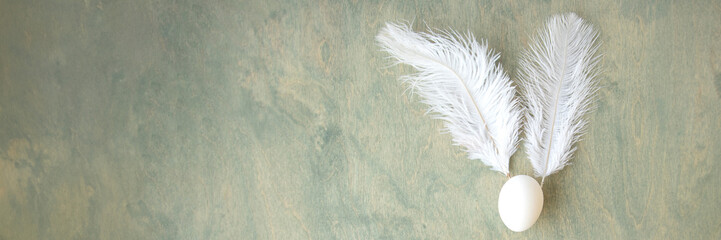 banner of Easter background, egg and white feathers in the form of a hare on a green wooden...