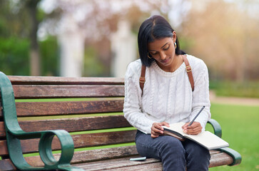 Indian girl, student and writing notes at park for education, learning or studying at university on...