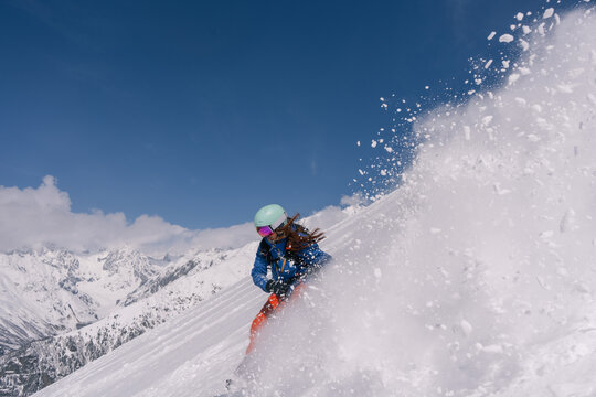 Woman snowboarder riding on slope of powdery snow in high mountains. Freeride at ski resort, Snow splashes trail,  mountain peaks view