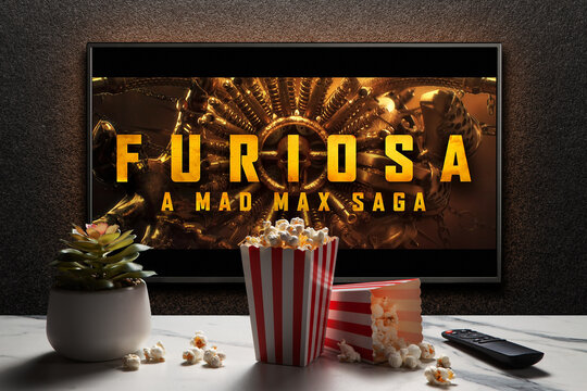 Furiosa A Mad Max Saga trailer or movie on TV screen. TV with remote control, popcorn boxes and home plant. Astana, Kazakhstan - April 18, 2024.