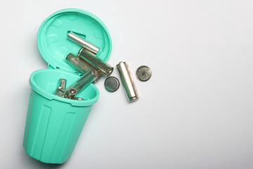 Thought-provoking photo of finger batteries in a mini bin, showcasing the need for proper disposal methods to protect our environment. on a white background.