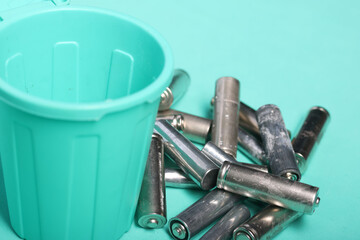 Used finger batteries near a miniature trash can. Light green background. Close-up.