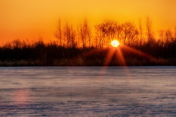Spring landscape. Sunrise of the solar disk over the northern icy river, on the bare winter floodplain forests. Northeast of Europe