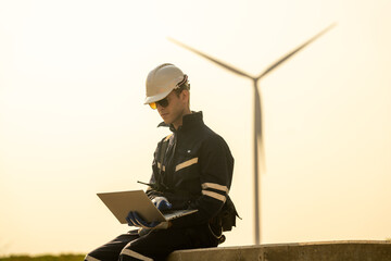 An engineer evaluates performance next to an immense wind turbine during a tranquil sunset. - obrazy, fototapety, plakaty