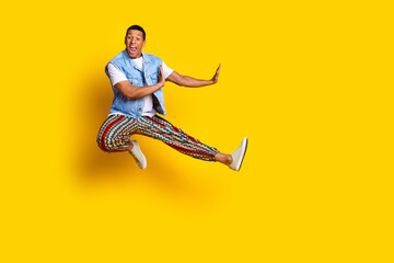Fototapeta na wymiar Full length photo of crazy eccentric guy dressed jeans waistcoat jumping near offer empty space isolated on yellow color background