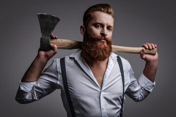Brutal mature bearded man with redhead beard and moustache in retro suspenders hold axe isolated on grey - 788530086