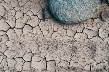 A close up of a large boulder sits on top of a dry, cracked earth. Cracked earth background