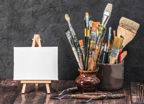 Creative composition with miniature canvas on an easel and vintage paint brushes on a wooden table. Artistic creativity concept.