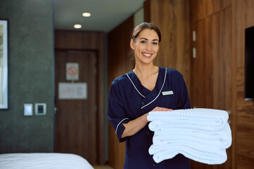 Happy chambermaid with fresh towels in hotel room looking at camera.