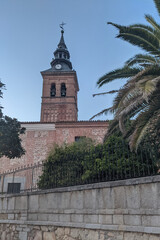 Catholic church in the historic Spanish town of Navalcarnero near Madrid. Bell tower with clock against a sky background and palm. Religion and culture in Europe - obrazy, fototapety, plakaty