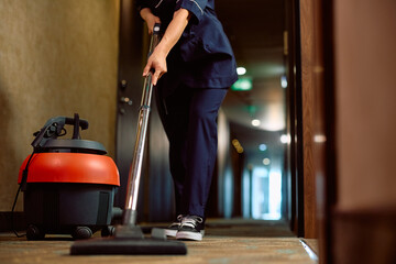 Close up of woman vacuuming hallway while working as maid in  hotel.