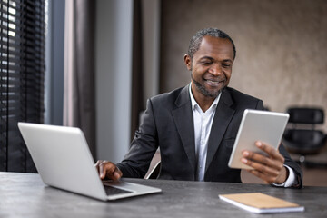 Smiling male in white shirt and black jacket using two electronic gadgets for optimisation of working process. Contemporary entrepreneur connecting to crm system of company for online interacting.