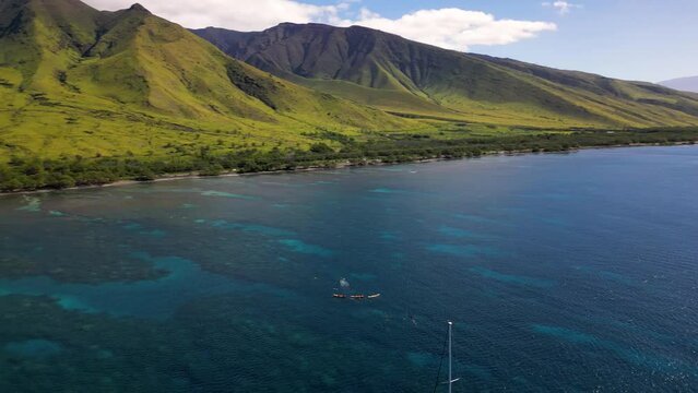 Tourists on kayaks and sailing boat exploring coral reefs on iconic mountainous coast of Maui, Hawaii. 
