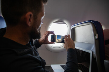 man taking photos through plane window