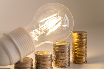 Light bulb lit, above stacks of coins. Increase in electricity tariffs, energy dependence, energy...