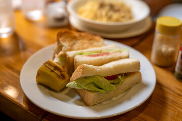 A plate with a classic sandwich and Japanese tamagoyaki omelette, served on a wooden table, ideal for a quick meal.