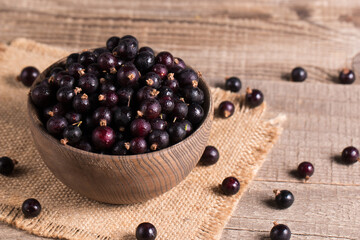 Black currant in a bowl on wooden background. Organic berries. 
