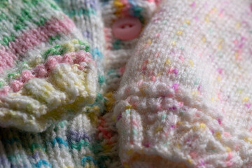 knitting background - hand knit baby cardigan in pink and green pastel colours with buttons 