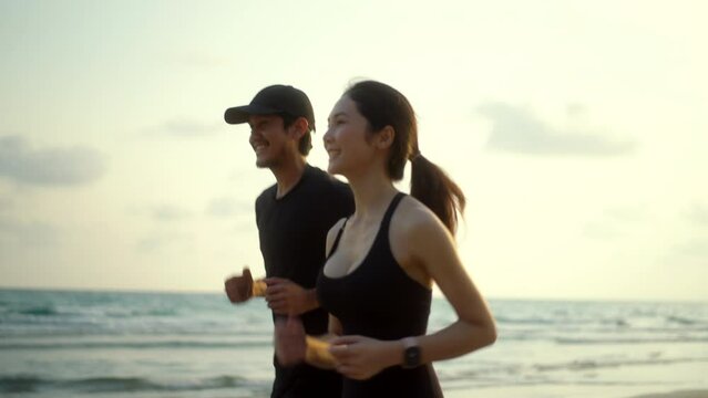 Young couple wearing sportswear running on sand sea ocean beach outdoor. Couple young two friends running or jogging at seaside for healthy lifestyle. Training athlete work out outdoor concept.