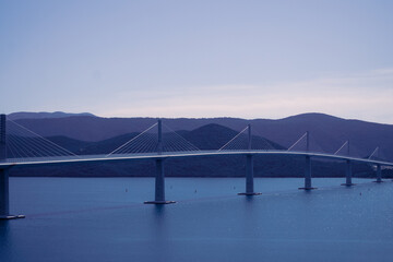 bridge over the sea at sunset, purple evening light, and forested hills in the background