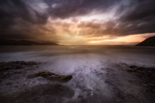 Sunset on the Lastron nudist beach in Zierbena, Bizkaia, with the water between the rocks on the shore