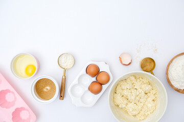 Bowl with dough, eggs , bowl of sugar, silicone molds ingredients on white background.