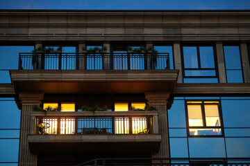 Glass facade buildings with balconies, light burns in one window. Windows and balconies