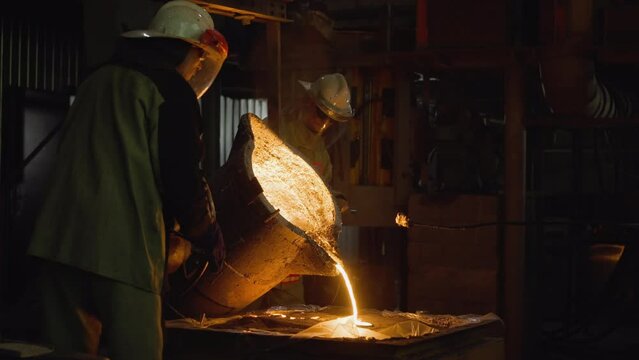 Team of foundry workers pouring glowing molten iron from ladle into molds