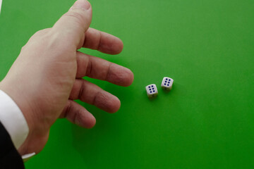 A man’s hand in a jacket throws two dice on a green cloth, two winning dice, the maximum number...