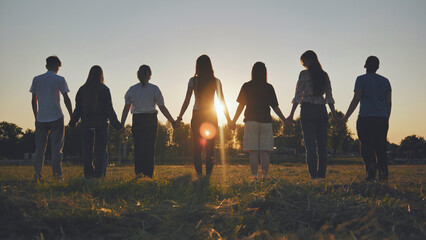 Friends standing holding hands at sunset.