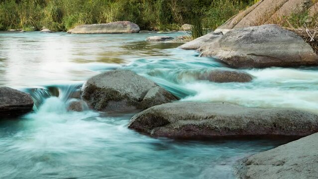The water flows turquoise through the big rocks on the riverside, the sky is clear and the light is soft 4K