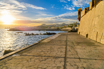 Sunset view of the coastline, town and bay from the São Tiago Fort, or Yellow Fort, at the seaside city of Funchal, Portugal, on the Canary Island of Madeira in the Atlantic Ocean.