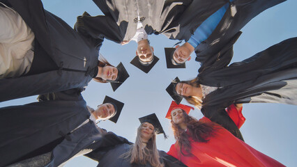 College graduates in a circle stand hugging each other.