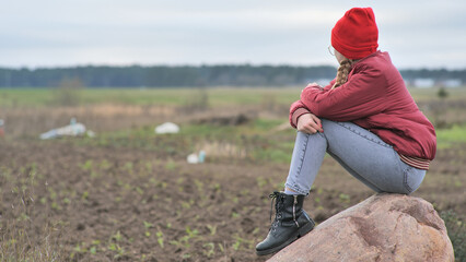 A sad teenage girl sits on a rock in a field and cries.
