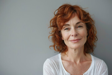 A woman with red hair is smiling and wearing a white shirt