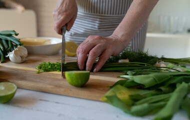 Woman cutting chives on a wooden cutting board in the kitchen