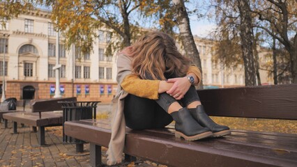 A young girl crying on a park bench in the fall.