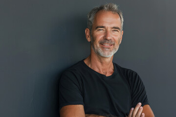 A man in a black shirt is smiling with his arms crossed