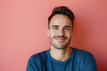 A man in a blue shirt is smiling in front of a pink wall