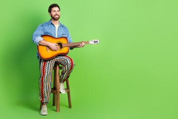 Full length photo of cheerful cool guy wear denim jacket sing enjoy guitar music looking empty space isolated green color background