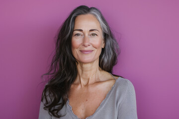 A woman with gray hair is smiling in front of a purple background