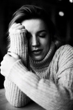 Engrossed in thought, a woman wearing a cozy sweater rests her head on her hand, seated at a table. The image captures a moment of deep contemplation and introspection. Contemplative Pause