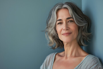 A woman with gray hair is leaning against a blue wall