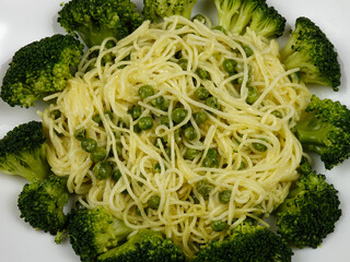 Italian spaghetti with green peas, broccoli and grated cheese parmesan lie on a white plate 